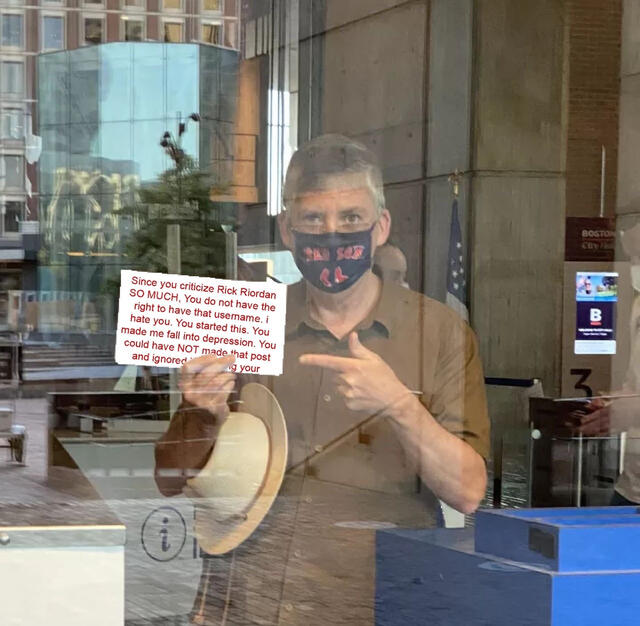 rick riordan pointing to a sign edited to with the text from a hate anon